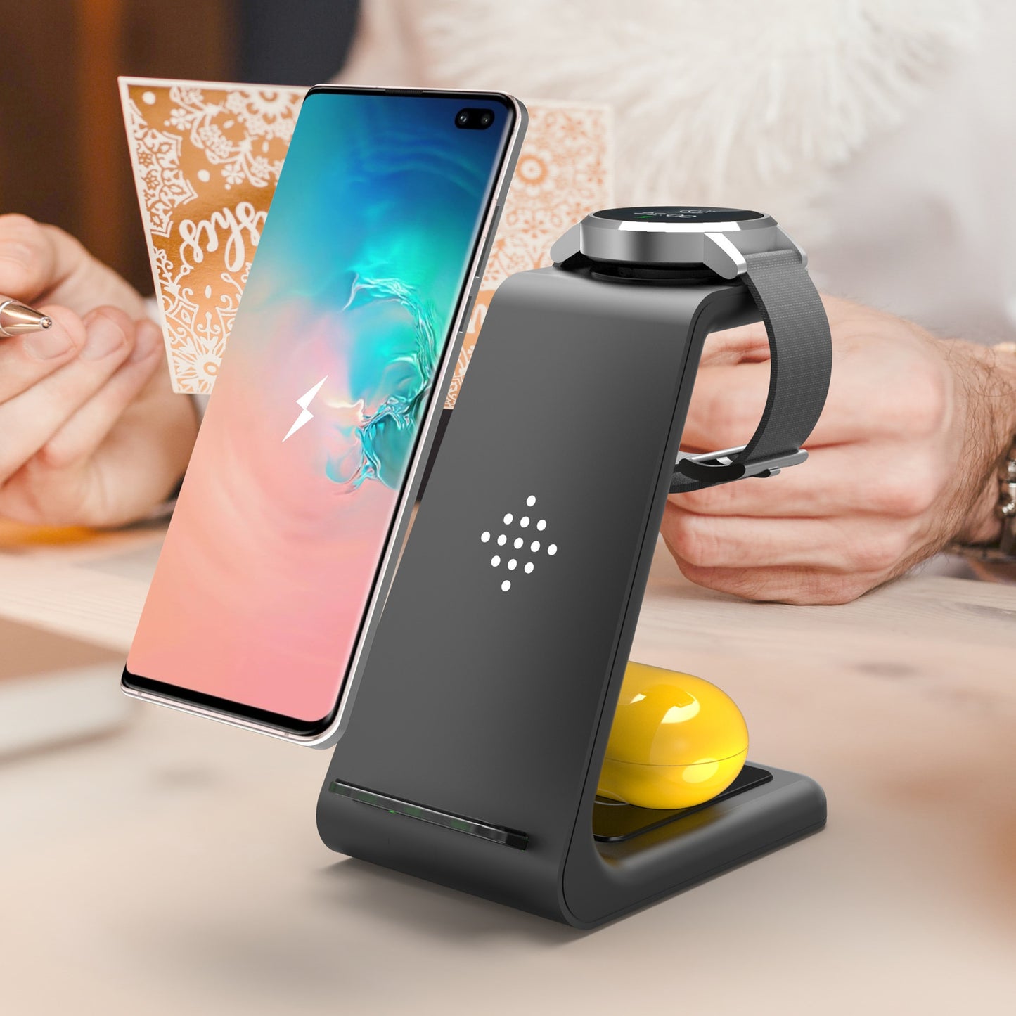 Black wireless charging stand with smartphone, smartwatch, and yellow ball on a blurred background