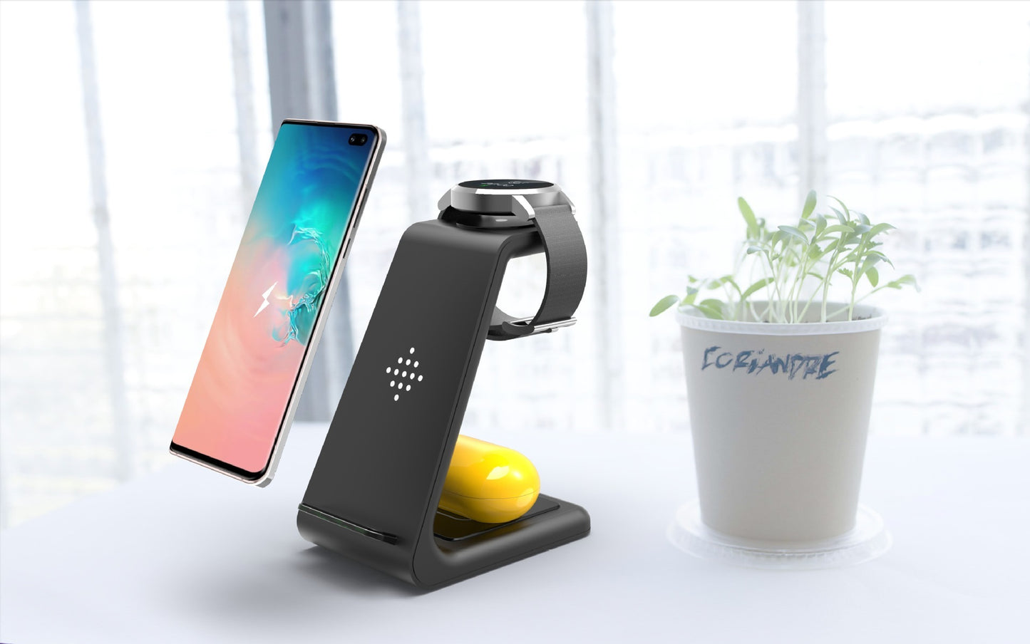 Black smartphone stand with a smartphone, smartwatch, and lemon on a white surface with a plant in the background.