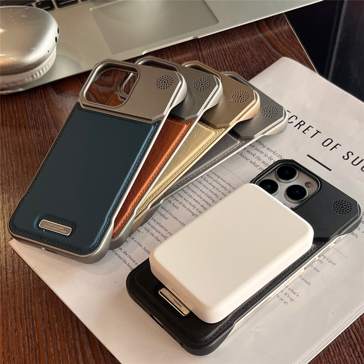 Four phone cases in different colors on a magazine with a laptop in the background
