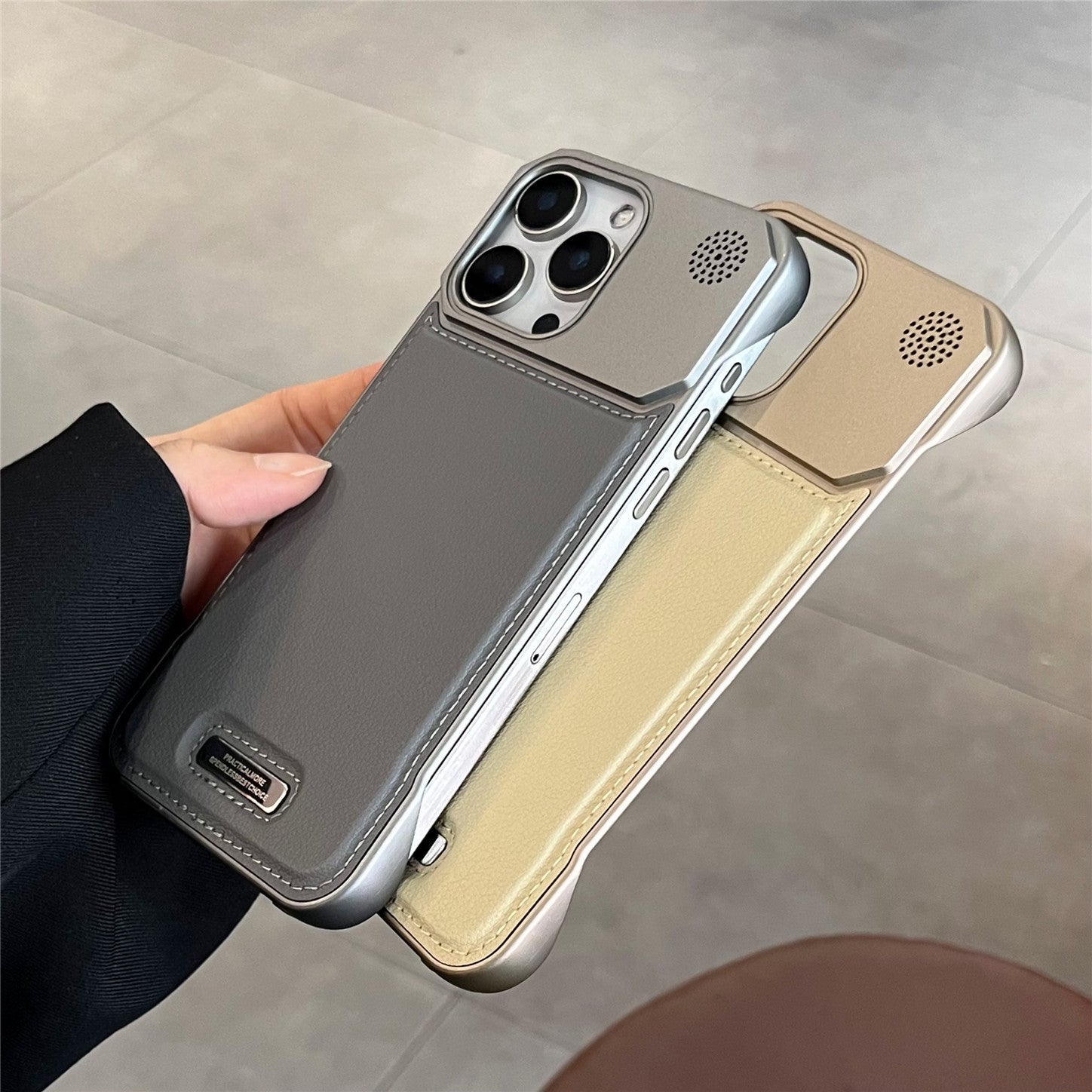 Two phone cases, one gray and one beige, held by a hand on a tiled floor.